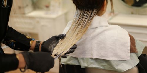 A woman sitting in a salon chair, getting her hair colored by a stylist.