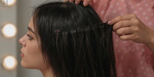 A woman is having her hair styled with a clip while adding hair extensions for extra volume.