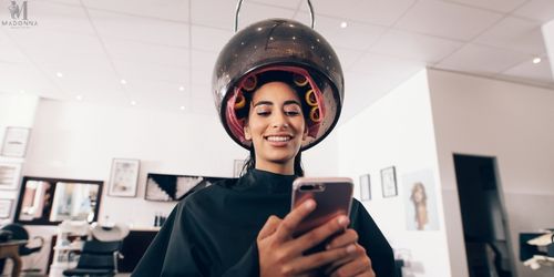 A smiling woman at a hair spa, holding her cell phone and enjoying her time.