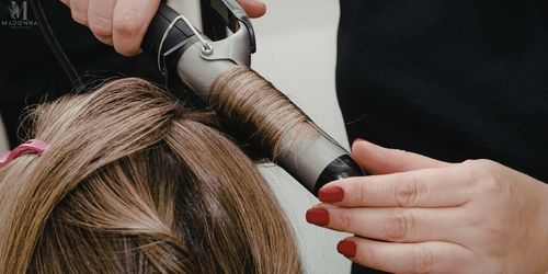 A hairstylist using a curling rod to style a woman’s hair.