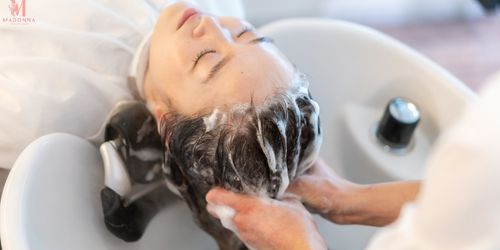 A woman enjoys a hair wash in a salon, reclining comfortably as water flows over her hair.