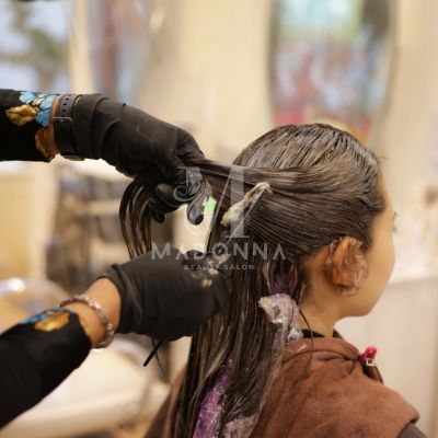 Hair Colour Salon in Mississauga A woman is sitting in a salon chair while a stylist is coloring her hair.